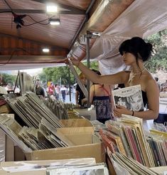 a woman is looking through records at an outdoor flea market with lots of books on display