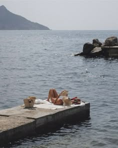 two people are laying on a dock in the middle of the water and one person is wearing a hat