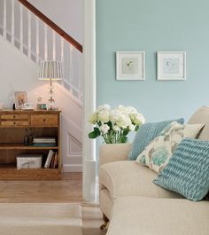 a living room filled with furniture next to a stair case and white flowers on top of a table