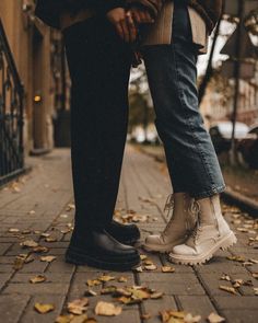 two people standing next to each other on a sidewalk with leaves all over the ground