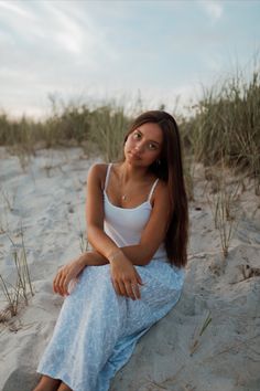 a woman is sitting on the sand with her legs crossed and looking at the camera