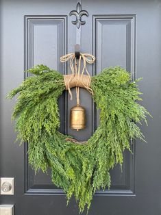 a wreath is hanging on the front door with a gold bell and greenery around it