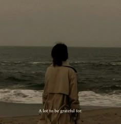 a woman standing on top of a beach next to the ocean with a message written in front of her