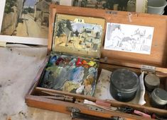 an open wooden box filled with lots of paint and other art supplies on top of a table