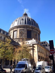 an old building with a cross on top and cars parked in the street below it