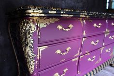 a purple and gold painted dresser sitting on top of a wooden floor