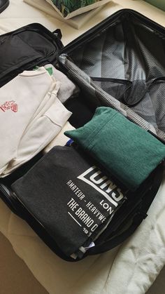 an open suitcase filled with clothes on top of a white bed next to a potted plant