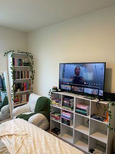 a flat screen tv sitting on top of a white book shelf next to a bed