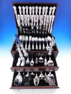 an assortment of silverware is displayed in a wooden display case on a blue background