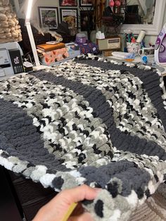 a person is holding up a crocheted blanket in front of a sewing machine