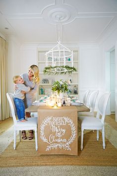 a woman holding a child in front of a table with candles on it and a sign that says merry christmas