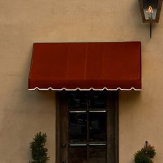 a cat sitting on the ground in front of a window with a red awning