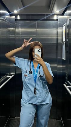 a woman in scrubs taking a selfie with her cell phone while standing in an elevator