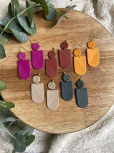 six pairs of leather earrings sitting on top of a wooden table next to eucalyptus leaves