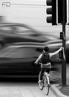 a woman riding a bike down a street next to a traffic light with cars in the background