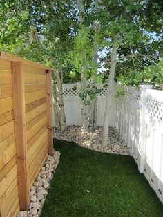 a wooden fence next to a lush green yard with rocks on the ground and trees in the background