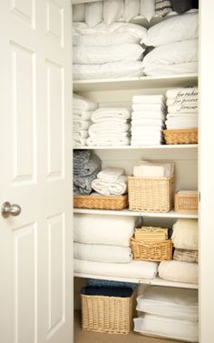 an organized closet with folded towels, baskets and linens on shelves next to the door