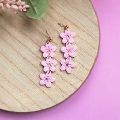 pink flowers are hanging from the side of a wooden plate on a purple surface next to a green plant