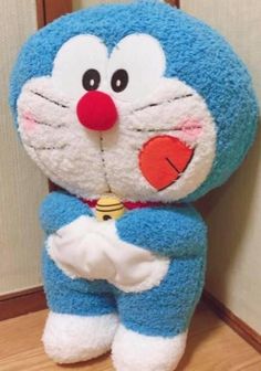 a blue and white stuffed animal sitting on top of a wooden floor next to a wall