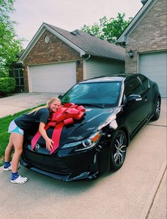 a woman is leaning on the hood of a black car with a red ribbon wrapped around it