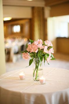 a vase filled with pink flowers sitting on top of a white table covered in candles