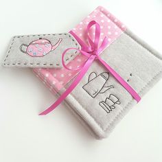 two small wallets with pink ribbon tied around them on a white surface, one has an elephant and the other has a teapot