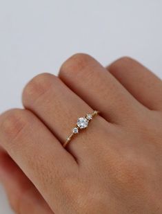 a woman's hand wearing a gold ring with three diamonds on it and the middle finger