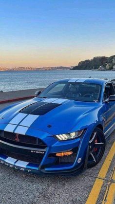 a blue sports car parked on the side of the road next to the water at sunset