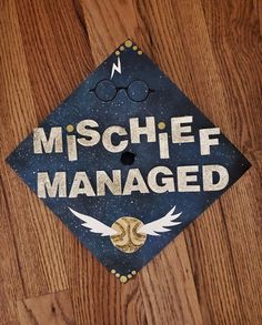 a blue cap with the words mischef managed on it sitting on top of a wooden floor