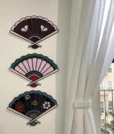 three decorative wall hangings on the side of a white wall next to a window