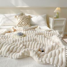 a large white blanket on top of a bed covered in pillows and pom poms