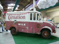 an old pink and white milk truck parked in a building with people standing around it