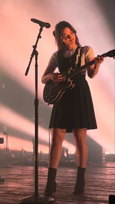 a woman standing in front of a microphone while holding a guitar