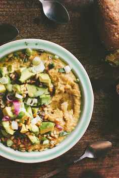 a bowl filled with food sitting on top of a wooden table next to spoons