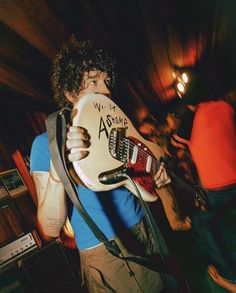 a man holding a guitar in his right hand and wearing a blue shirt with writing on it