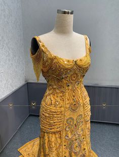 a yellow dress on display in a room with grey walls and flooring, it has an elaborately beaded neckline