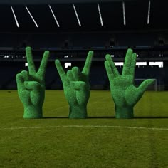 three large green hand sculptures in the shape of fingers on a soccer field at night