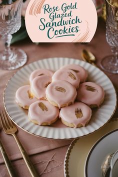 pink glazed sandwich cookies on a white plate with gold rimmed forks and silverware