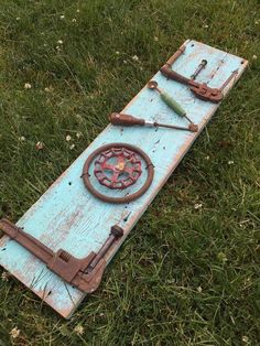 an old blue board laying in the grass with tools attached to it and two wrenches on top