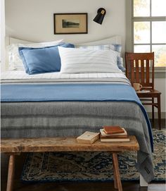 a bed with blue and white sheets in a bedroom next to a wooden bench near a window