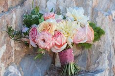 a bouquet of pink and white flowers sitting on top of a rock wall next to a stone wall