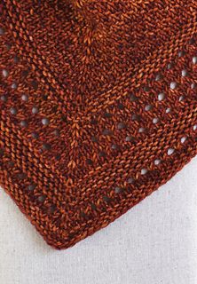 an orange knitted square on top of a white cloth with holes in the middle