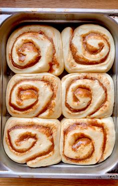 several cinnamon rolls in a metal pan on a wooden table