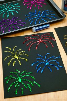 fireworks on black paper next to a cookie sheet with crayons and paintbrushes