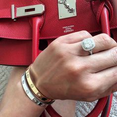 a woman's hand holding a red purse with a white diamond ring on it