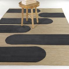 a rug with black circles on it and a stool next to it in front of a white wall