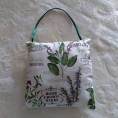 a white bag with flowers and herbs printed on the front, hanging from a green ribbon