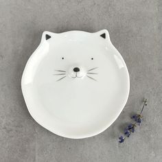 a white plate with a cat's face on it and lavenders in the background