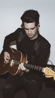 a man is playing an acoustic guitar while sitting on a couch in front of a white wall