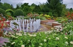 a garden filled with lots of different types of flowers and water fountains surrounded by greenery